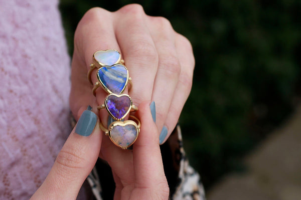 Model holding 18k gold opal heart rings for October birthdays by Los Angeles fine jewelry designer Brooke Gregson